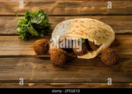 Le palle di falafel in una pita e prezzemolo fresco verde su uno sfondo di legno.Falafel svolge un ruolo iconico nella cucina israeliana ed è ampiamente considerato come il piatto nazionale del paese. Foto Stock