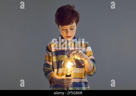 Ragazzo che tocca una lampadina incandescente nel supporto di mano isolato su spazio copia studio Foto Stock