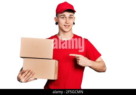 Ragazzo caucasico giovane con le orecchie dilatazione tenendo il pacchetto di consegna sorridente buon puntamento con mano e dito Foto Stock