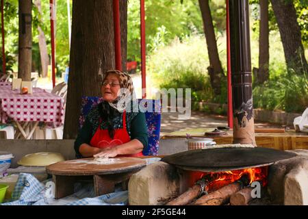 ANTALYA, TURCHIA - 30 maggio 2015 : tradizionalmente vestita Vecchia donna è makingTurkish frittelle sul fuoco nel Parco. Foto Stock