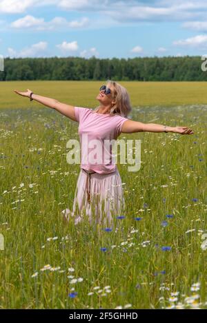 Una donna di mezza età in un campo di fiori, godendosi l'estate, gioendo al sole. Foto Stock