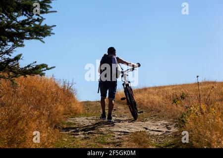 Un ciclista che spinge una bicicletta in salita Foto Stock