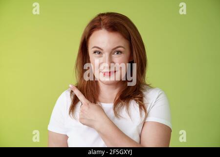 Gentile allegra buona-osservante metà-invecchiata donna 50s rosso-testa bianca t-shirt sorridente modesto garantito dare consigli che indicano in alto a sinistra angolo indica grande Foto Stock