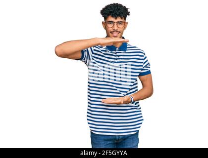 Giovane arabo che indossa abiti casual e occhiali che gesturano con le mani che mostrano grande e grande segno di misura, misura simbolo. Sorridendo guardando la fotocamera. Foto Stock