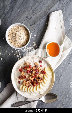 Colazione a base di cereali sani, farinata d'avena con fette di banana, mirtilli rossi secchi, noce, servita con miele in una ciotola Foto Stock