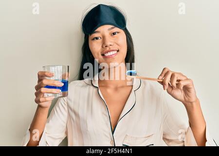 Giovane donna cinese che indossa il pajama usando lo spazzolino da denti e il boccaglio sorridendo con un sorriso felice e fresco sul viso. Mostrando i denti. Foto Stock