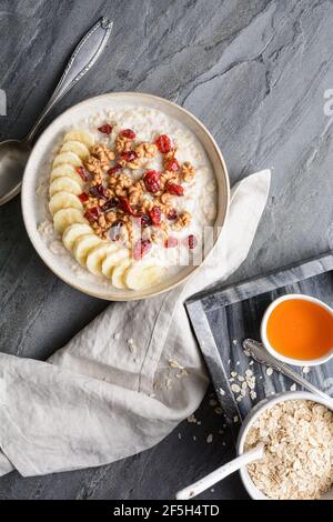 Colazione a base di cereali sani, farinata d'avena con fette di banana, mirtilli rossi secchi, noce, servita con miele in una ciotola Foto Stock