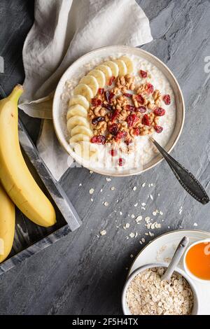 Colazione a base di cereali sani, farinata d'avena con fette di banana, mirtilli rossi secchi, noce, servita con miele in una ciotola Foto Stock