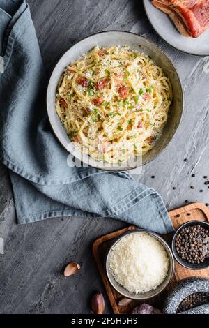 Pasta classica Carbonara in un piatto di ceramica, sostanzioso piatto italiano a base di spaghetti, uova, pancetta fritta, condito con parmigiano grattugiato e pe nero Foto Stock