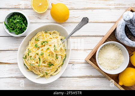 Pasta al Limone, delizioso pasto italiano, spaghetti al parmigiano, burro e salsa al limone, conditi con scorza grattugiata fresca e formaggio su rustica macina di legno Foto Stock