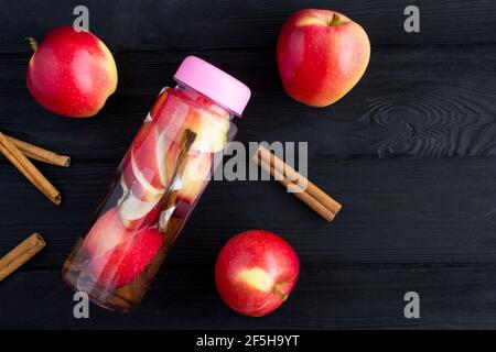 Infuso o detox acqua con mela e cannella in bottiglia su fondo nero di legno. Vista dall'alto. Spazio di copia. Foto Stock