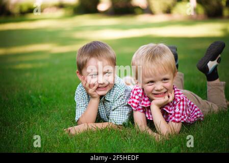 Due fratelli che giacciono sull'erba in un parco all'aperto, sorridenti e. Foto Stock