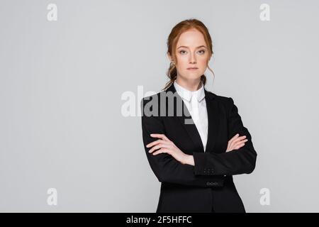 Donna d'affari dai capelli rossi in piedi con braccia incrociate isolate su grigio Foto Stock