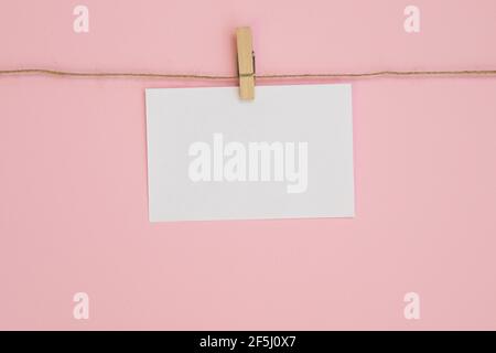 Foglio di carta vuoto per note, cornici che pendono su una corda con stendibiancheria e isolati su sfondo rosa. Bianco vuoto con spazio vuoto per il testo. Foto Stock