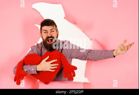 Uomo sorridente con cuscino a forma di cuore. Ragazzo bearded con cuscino rosso del cuore. Simbolo d'amore. Concetto di giorno di San Valentino. Foto Stock