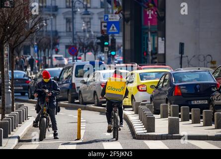 Bucarest, Romania - 08 marzo 2021: Un corriere di consegna di cibo di Glovo, vicino ad un corriere di consegna di pizza di Jerry, trasporta il cibo a Bucarest, Romania. Foto Stock