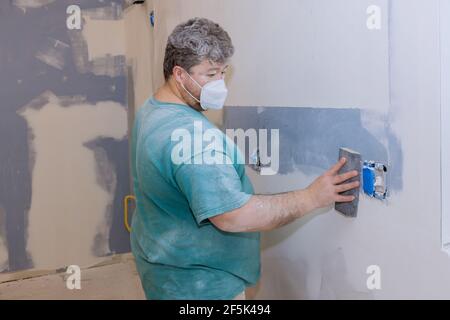 Il contraente che utilizza un cazzuola di sabbia levigando il muro a secco sulla parete Foto Stock