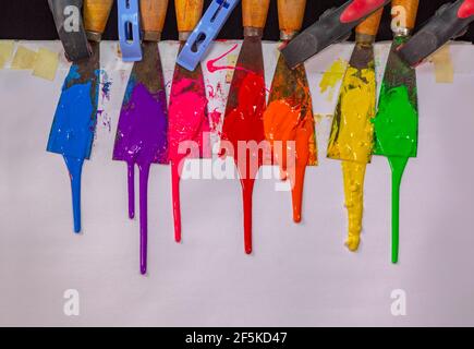 blu, viola, rosa, rosso, arancione, giallo e verde gocciolano lentamente dal manico del cucchiaio colorato e si spalmano lentamente sulla carta bianca. Foto Stock