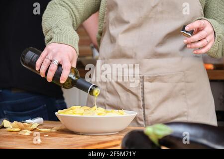 Giovane donna irriconoscibile che versa olio d'oliva su patate a fette. Tempo di cottura. Foto Stock