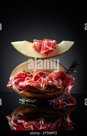 Prosciutto con melone e rosmarino su fondo nero riflettente. Foto Stock