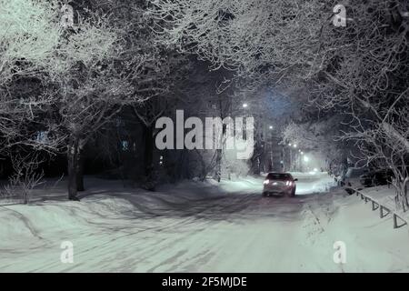 L'auto si muove lungo una strada innevata nel parcheggio di notte. Foto Stock