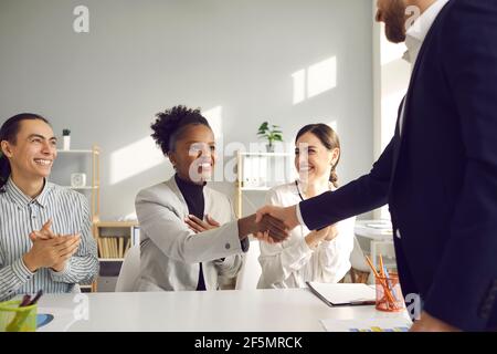 Donna felice sorridente e scuotente le mani con il suo partner commerciale riunione in ufficio Foto Stock