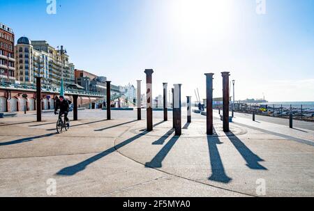 Brighton UK 27 marzo 2021 - UN ciclista gode di una luminosa mattina soleggiata ma fredda vicino alla spirale dorata sul lungomare di Brighton . Il tempo è previsto per girare molto più caldo la prossima settimana con temperature previste per raggiungere oltre 20 gradi in alcune parti del Regno Unito: Credit Simon Dack / Alamy Live News Foto Stock