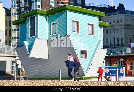 Brighton UK 27 marzo 2021 - UNA famiglia godersi una passeggiata oltre la casa capovolta in una mattinata soleggiata ma fredda lungo il lungomare di Brighton . Il tempo è previsto per girare molto più caldo la prossima settimana con temperature previste per raggiungere oltre 20 gradi in alcune parti del Regno Unito: Credit Simon Dack / Alamy Live News Foto Stock