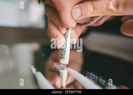 Primo piano di uomo che sniffing linee di cocaina su specchio attraverso banconota da dollaro arrotolata Foto Stock