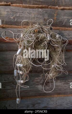 Una vecchia rete da pesca con galleggianti appesi su un muro di tronchi. Primo piano Foto Stock