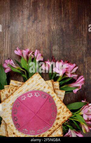 Pane matzah ebraico con kippah e fiori su sfondo di legno. Concetto di vacanza di passaggio. Foto Stock