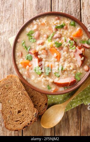 Zuppa slovena di orzo e fagioli con carne affumicata da vicino in un recipiente sul tavolo. Vista dall'alto verticale Foto Stock