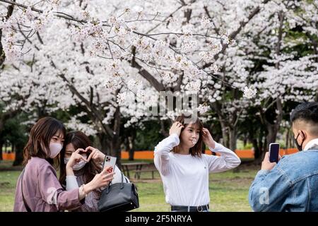 Tokyo, Giappone. 27 Marzo 2021. Le donne posano per delle foto accanto ai ciliegi in fiore (sakura) al Parco Yoyogi di Tokyo. L'area di Sakura è bloccata dalle linee arancioni per evitare che le folle si riuniscano nelle vicinanze. La gente gode la fioritura dei ciliegi da lontano. Il governo giapponese ha chiuso lo stato di emergenza il 21 marzo, ma ha esortato le persone a non riunirsi per prevenire una recrudescenza di infezioni da COVID-19. Credit: SOPA Images Limited/Alamy Live News Foto Stock