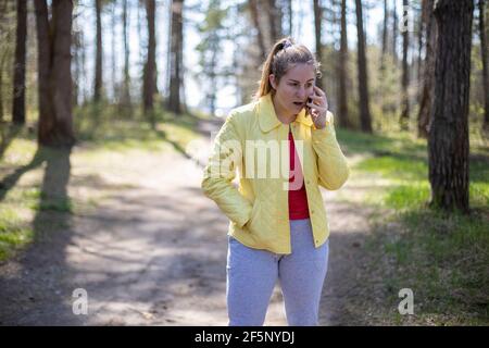 la donna nella foresta parla emotivamente al telefono. concetto di comunicazione cellulare 5g Foto Stock