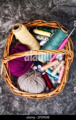 Cesto pieno di fili colorati e palle di filato e. un gancio a crochet Foto Stock