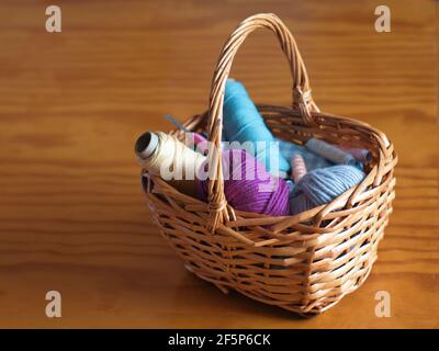 Cesto pieno di fili colorati e palle di filato e. un gancio a crochet Foto Stock