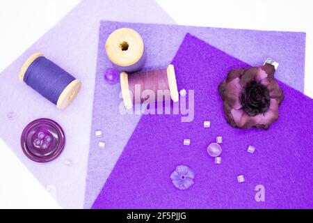 Articoli da cucire viola: Feltro in tre tonalità di lilla, bobine di legno con filo, perline, bottoni, e una rosa viola. Foto Stock