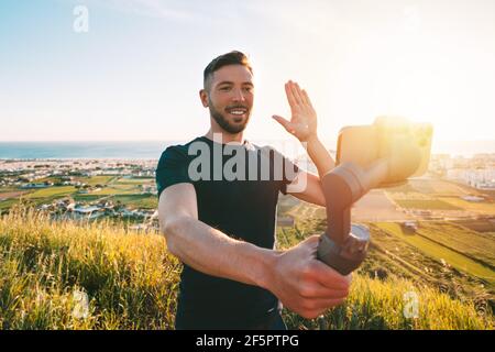 Uomo blogger registra video blog o in streaming dal vivo con il telefono e gimbal all'aperto Foto Stock