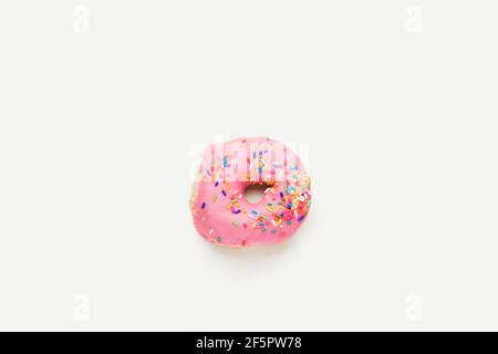 Vista dall'alto su una ciambella ad anello fresca con glassatura rosa e coloratissime spruzzette isolate su una superficie e uno sfondo bianchi. Foto Stock