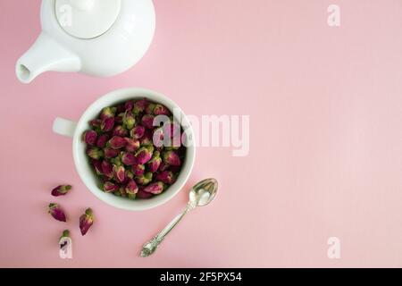 Asciugare le rose rosa nella tazza bianca e preparare il bollitore su sfondo rosa.Copia spazio.Vista dall'alto. Foto Stock