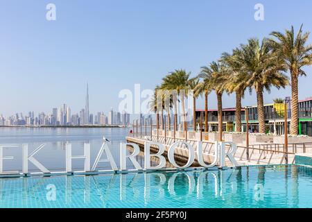 Dubai, Emirati Arabi Uniti, 22.02.2021. Cartello del Porto di Dubai Creek vicino alla piscina d'acqua turchese con file di palme e skyline del centro di Dubai sullo sfondo. Foto Stock
