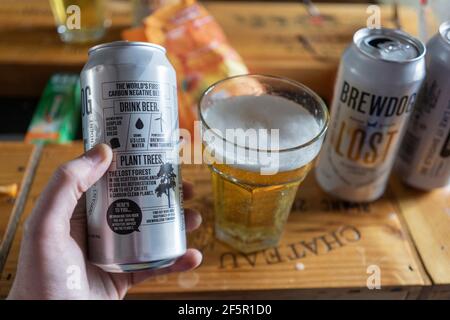 Una mano di un uomo che tiene in mano una lattina e un bicchiere di Brew Dog Lost Lager, una pilsner prodotta utilizzando l'energia eolica ed è la prima birra al mondo a emissioni di carbonio negative. Inghilterra Foto Stock