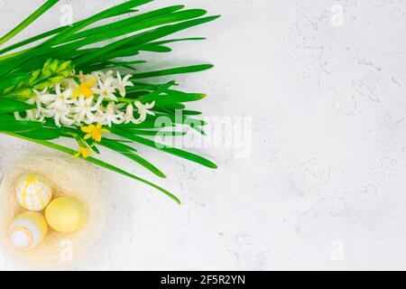 Concetto di primavera, Pasqua. Uova di Pasqua gialle in un nido accanto ad un bouquet di narcisi su un tavolo di cemento bianco. Luogo per un'iscrizione. La base per Foto Stock