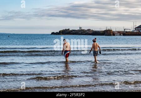 Due nuotatori maschi selvatici o in mare aperto con bauli da nuoto entrano nel Firth of Forth Sea a West Bay, North Berwick, East Lothian, Scozia, Regno Unito Foto Stock