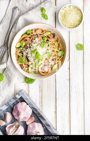 Sani spaghetti di grano integrale con aglio e zucchine di funghi saltati, conditi con formaggio grattugiato e foglie di basilico su rustico fondo di legno Foto Stock