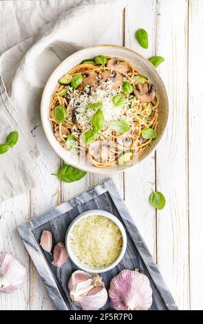 Sani spaghetti di grano integrale con aglio e zucchine di funghi saltati, conditi con formaggio grattugiato e foglie di basilico su rustico fondo di legno Foto Stock