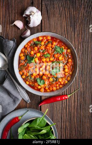 Pasto indiano, curry piccante di ceci con spinaci in una ciotola su rustico sfondo di legno Foto Stock