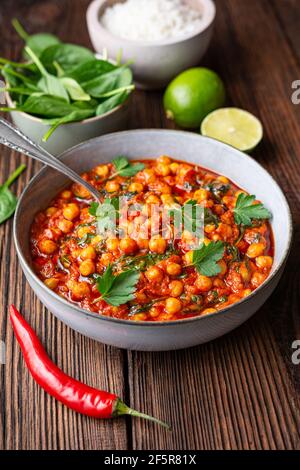 Pasto indiano, curry piccante di ceci con spinaci in una ciotola servita con riso su rustico fondo di legno Foto Stock