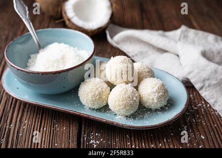 Deliziosa caramella senza forno, tartufi al cioccolato bianco ricoperti di cocco grattugiato su rustico sfondo di legno Foto Stock