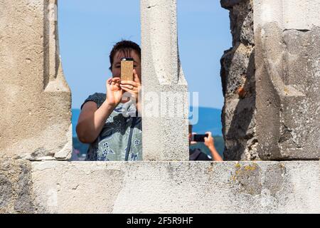 Donna che tiene uno smartphone per scattare foto attraverso la cornice di una finestra in pietra nel castello reale di Visegrad, Ungheria Foto Stock